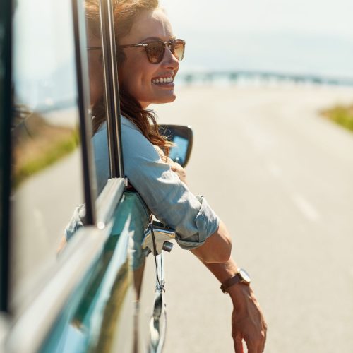 Cropped shot of an attractive woman hanging out of a car window while enjoying a road trip.